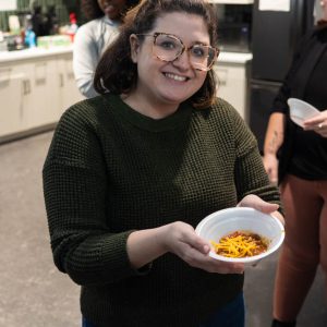 Woman holding bowl of chili with cheese.